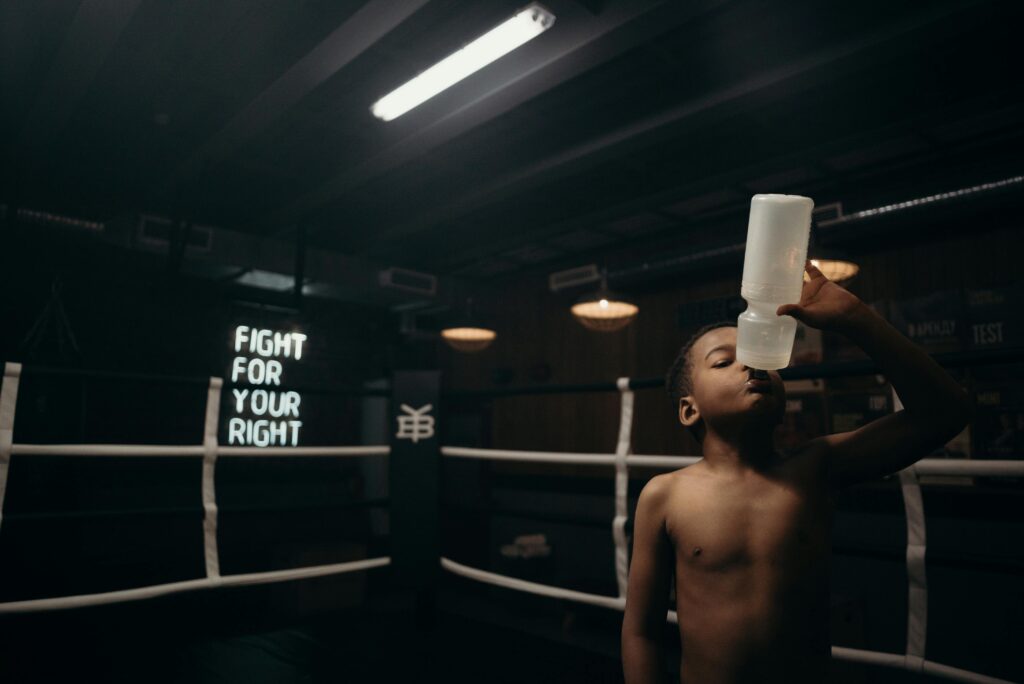 a boy drinking from a bottle in a boxing ring