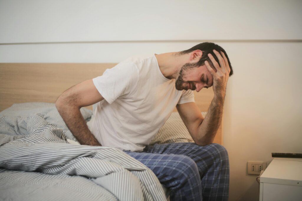 a sick man sitting on a bed with his hand on his head