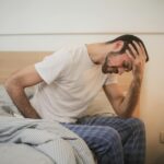 a sick man sitting on a bed with his hand on his head